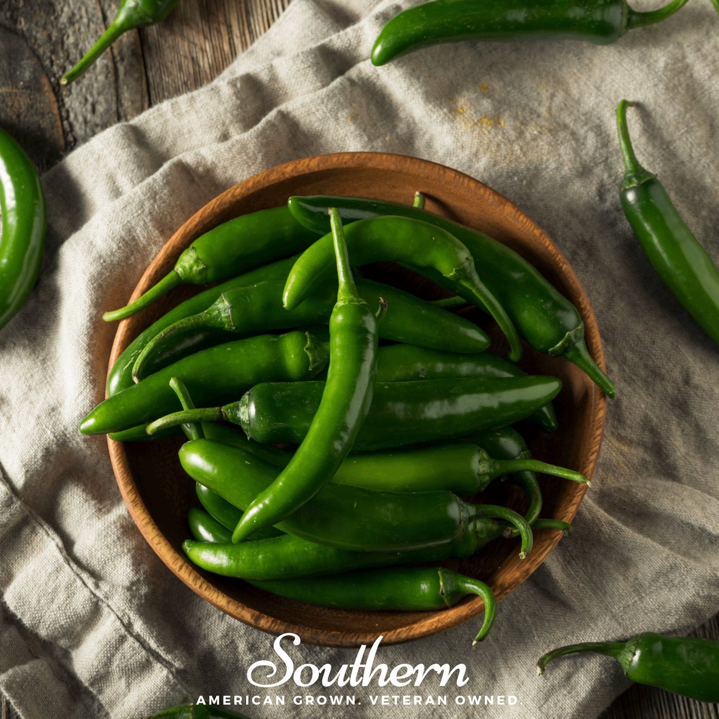 Wooden bowl filled with green chilies on a textured fabric background with 'Southern' branding.