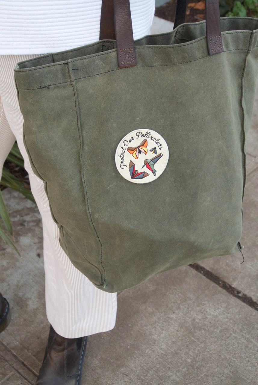 Green tote bag with a circular logo featuring butterflies on a neutral background