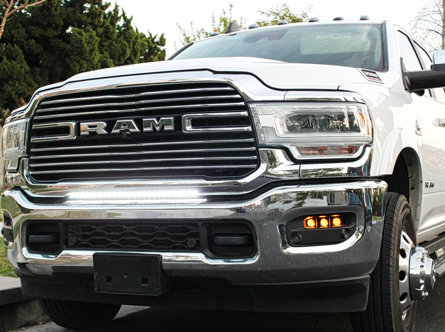 White Ram truck with chrome grille, light bar and headlights on a road.