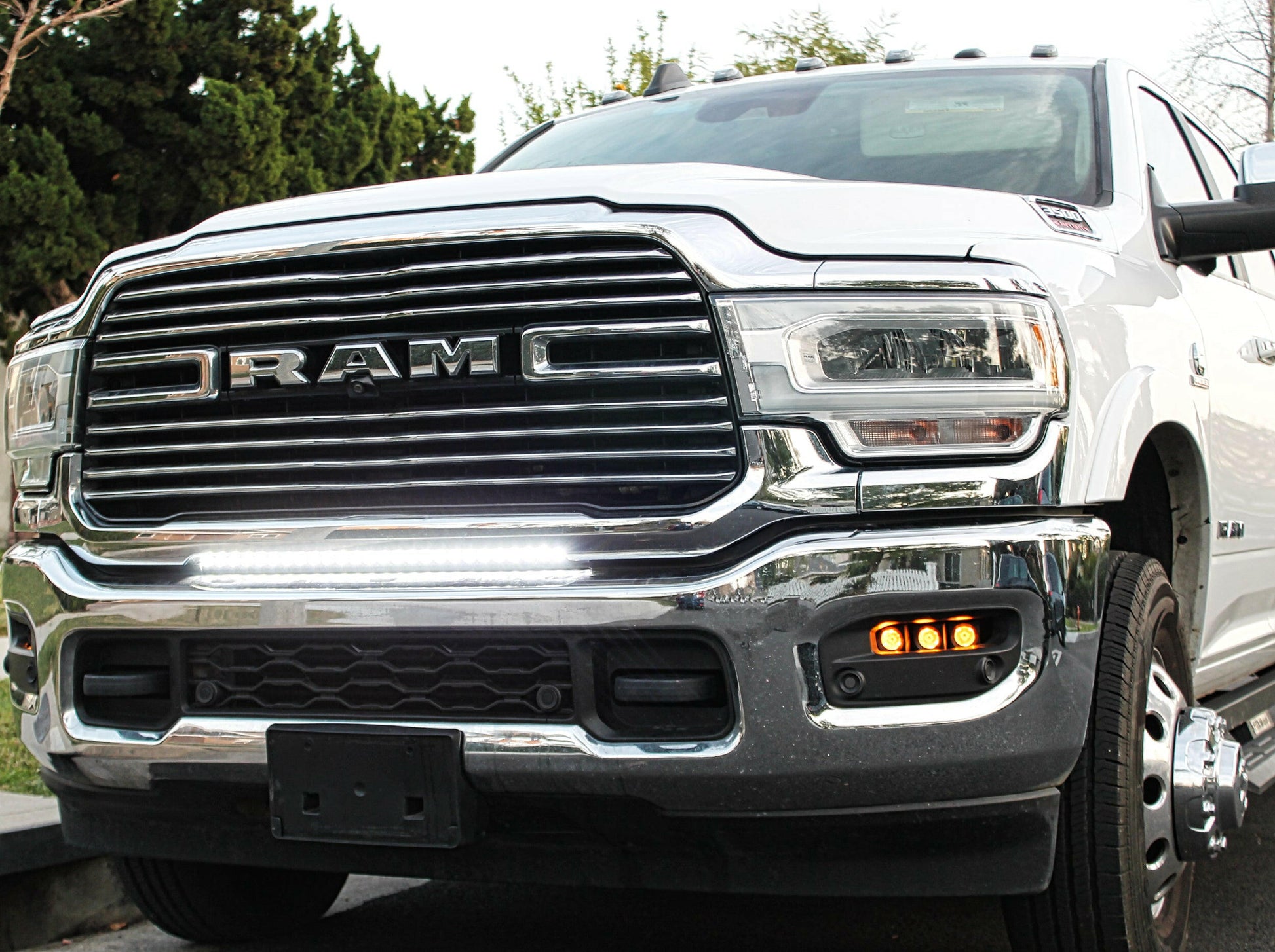 White Ram truck with chrome grille, light bar and headlights on a road.