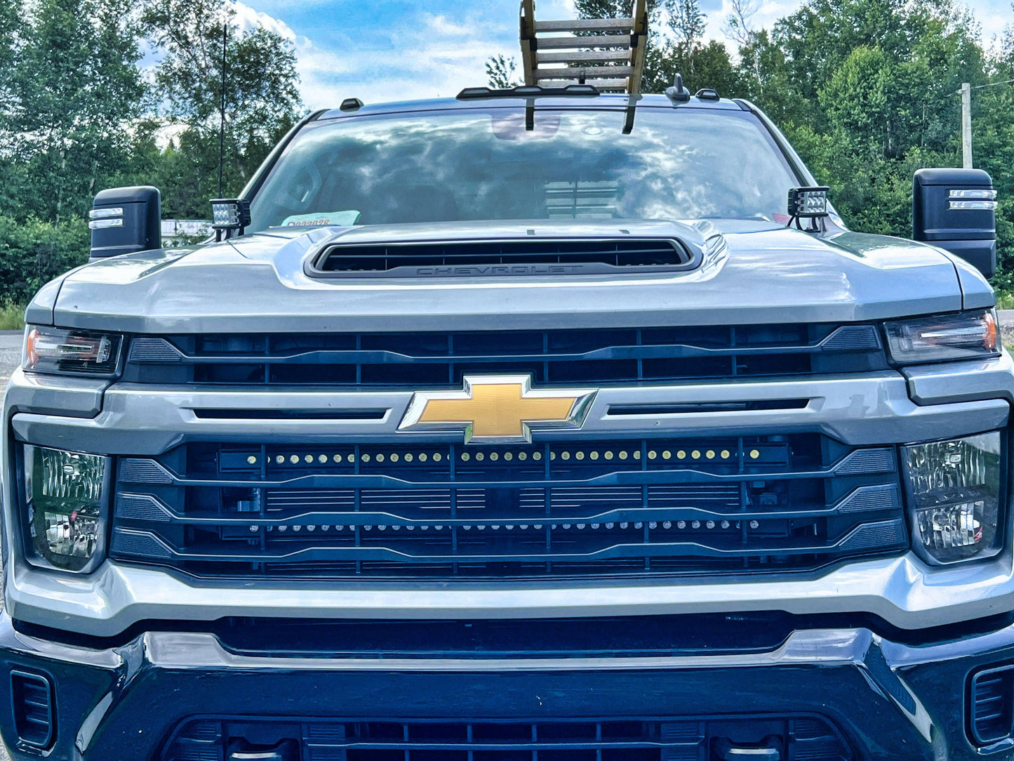 Front view of a Chevrolet truck with a clear sky and trees in the background