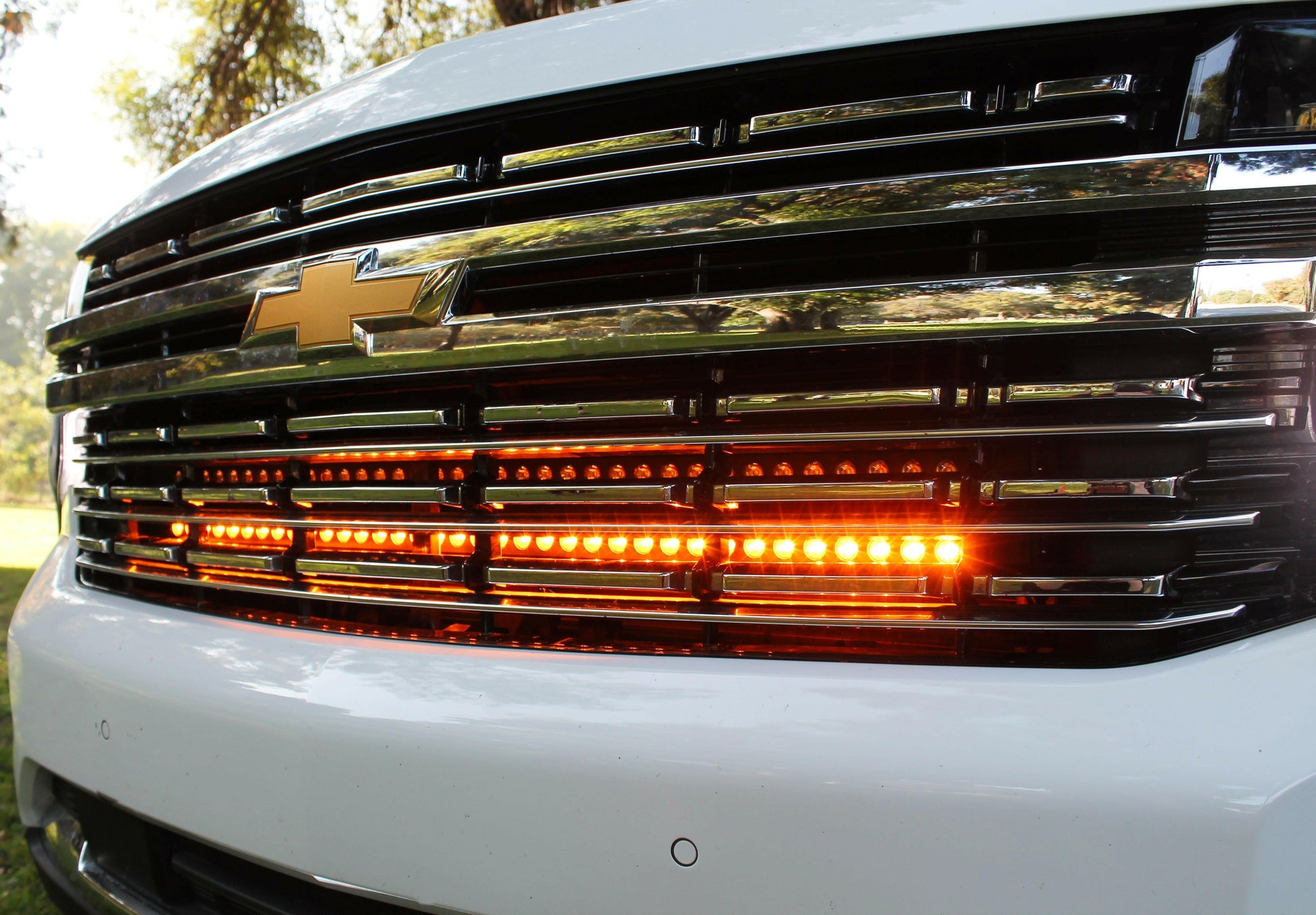 Close-up of a white truck's front grille with visible Chevrolet logo and Amber LED lights.