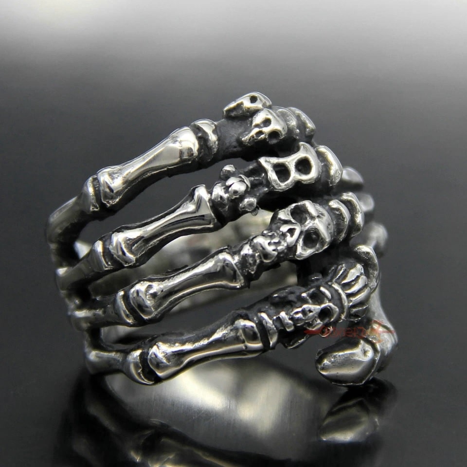 Silver skeleton hand ring on a reflective black surface