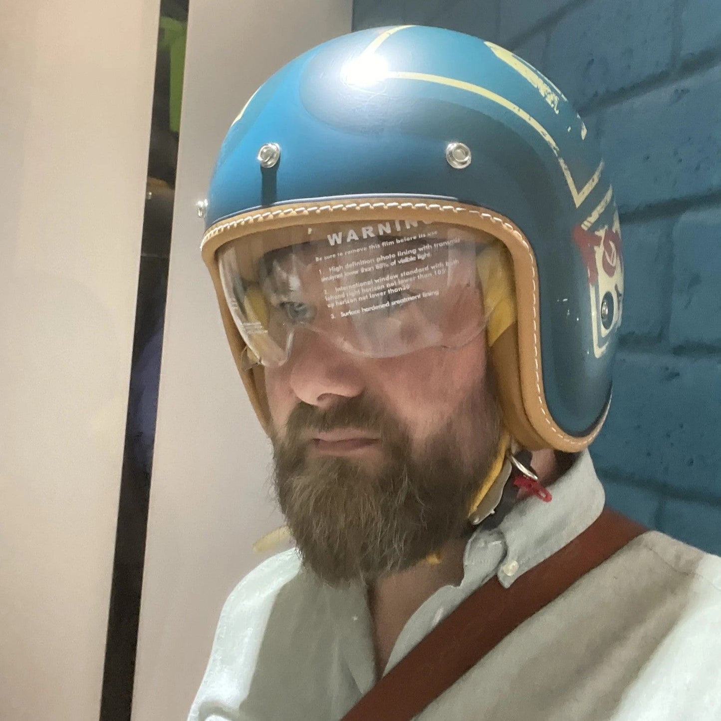 Man wearing a blue and yellow helmet with a clear visor against a blue brick wall.
