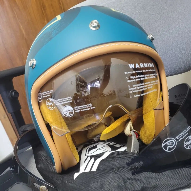 Close-up of a blue and beige motorcycle helmet with clear visor on a black bag.