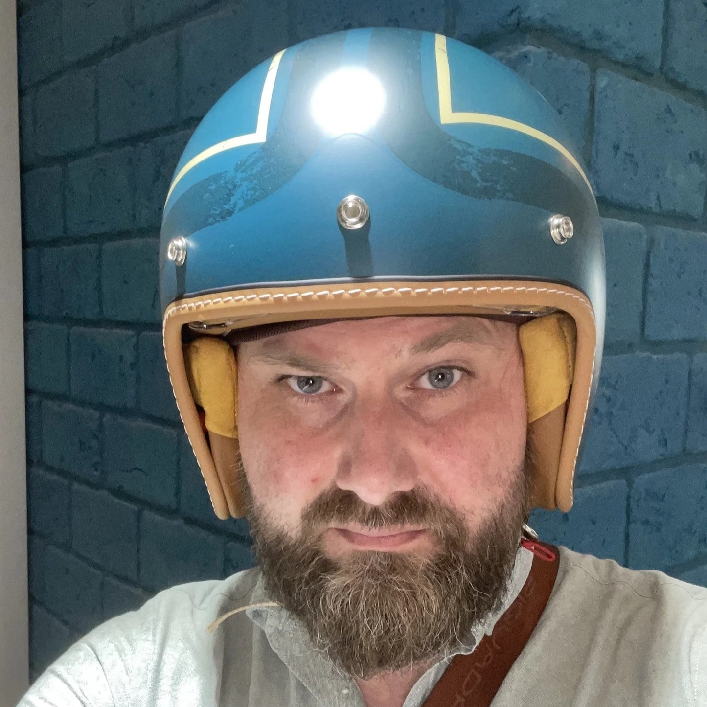 Man wearing a blue and beige helmet with a light on a blue brick wall background