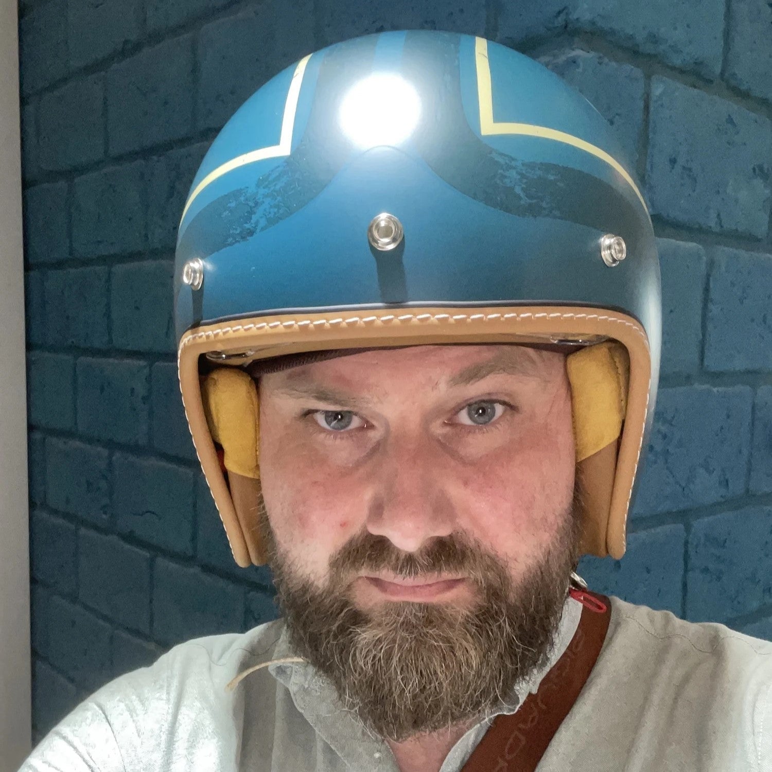 Man wearing a blue and beige helmet with a light on a blue brick wall background