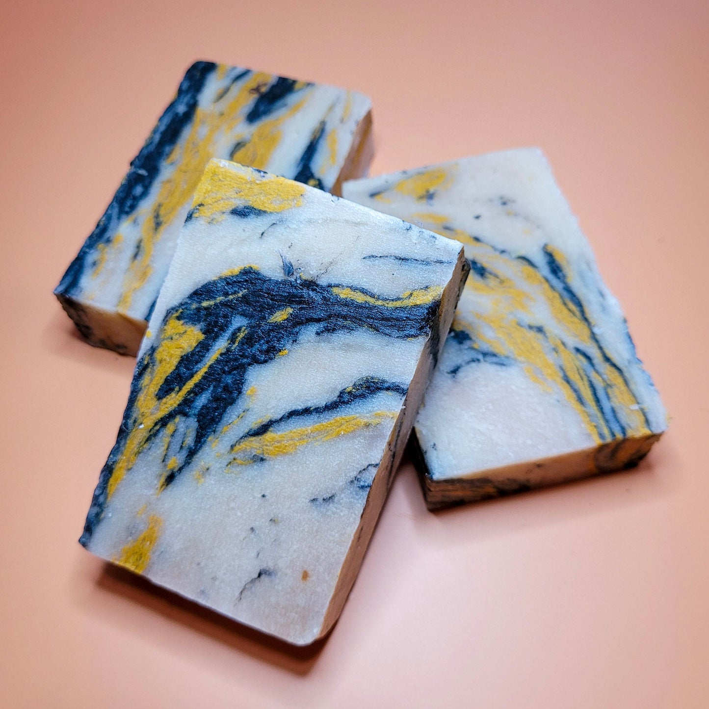 Three marbled soap bars with blue and yellow patterns on a peach background
