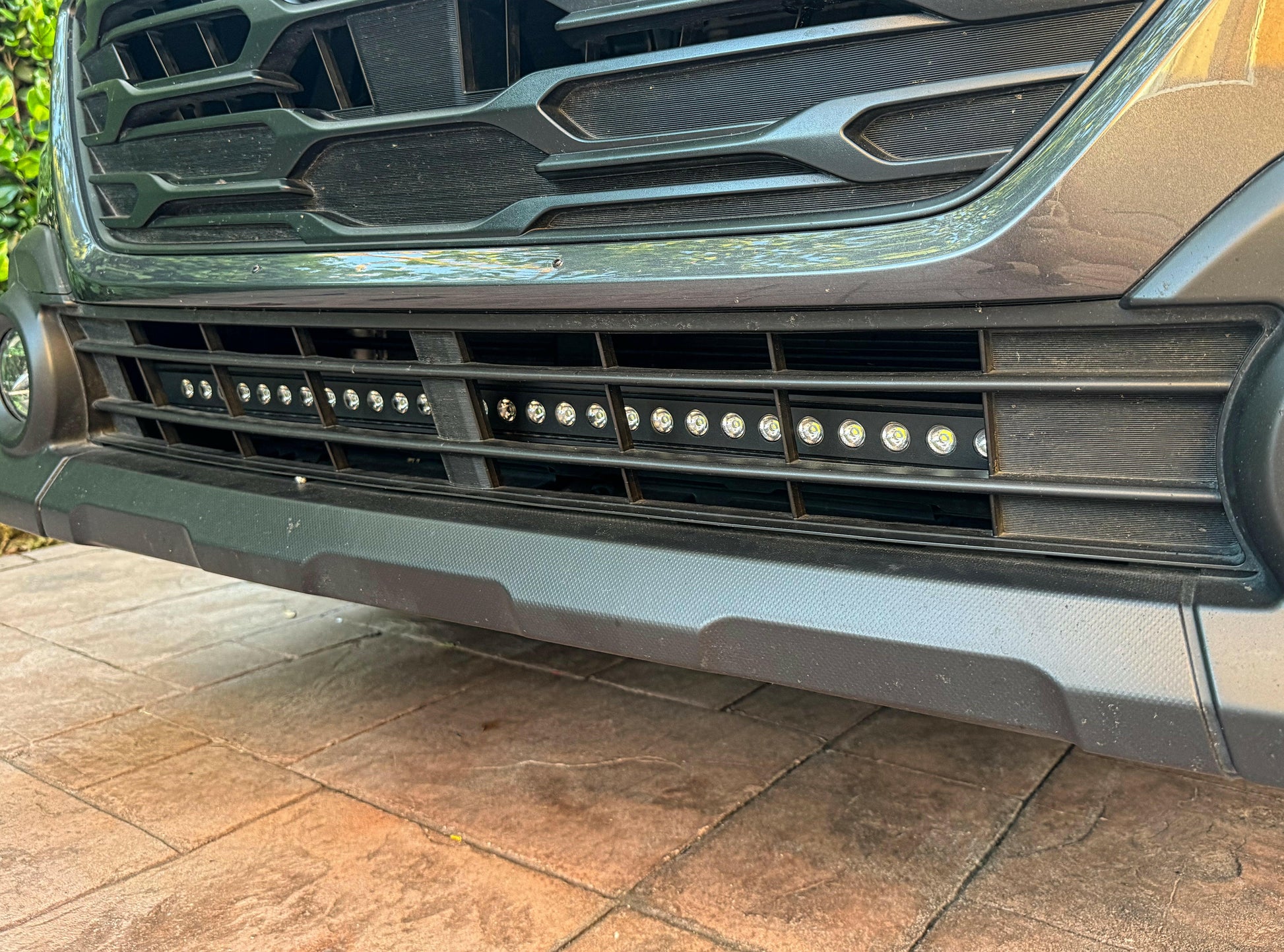 Close-up of a vehicle's front bumper with LED lights on a tiled floor.