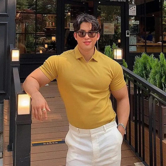 Man wearing a yellow polo shirt and white pants standing outdoors near a building entrance.