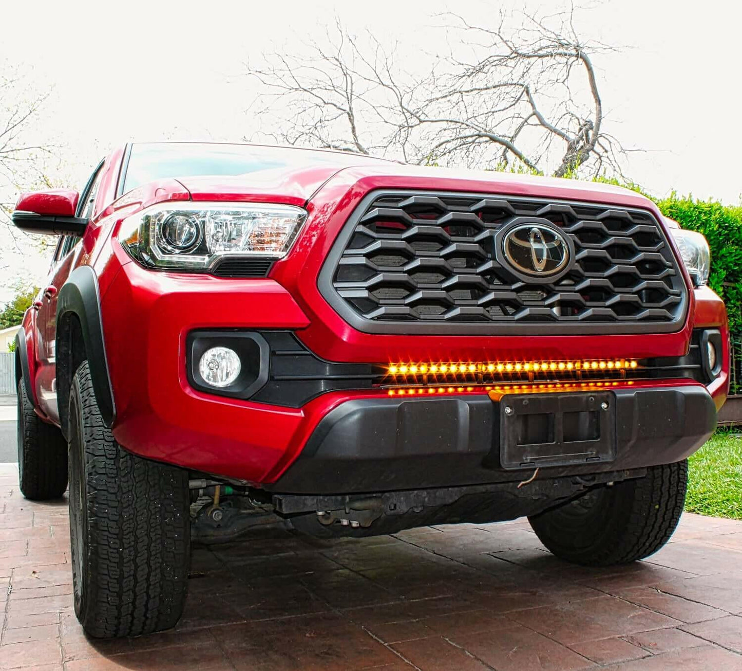 Red Toyota truck with a prominent front grille and LED light bar on a driveway.