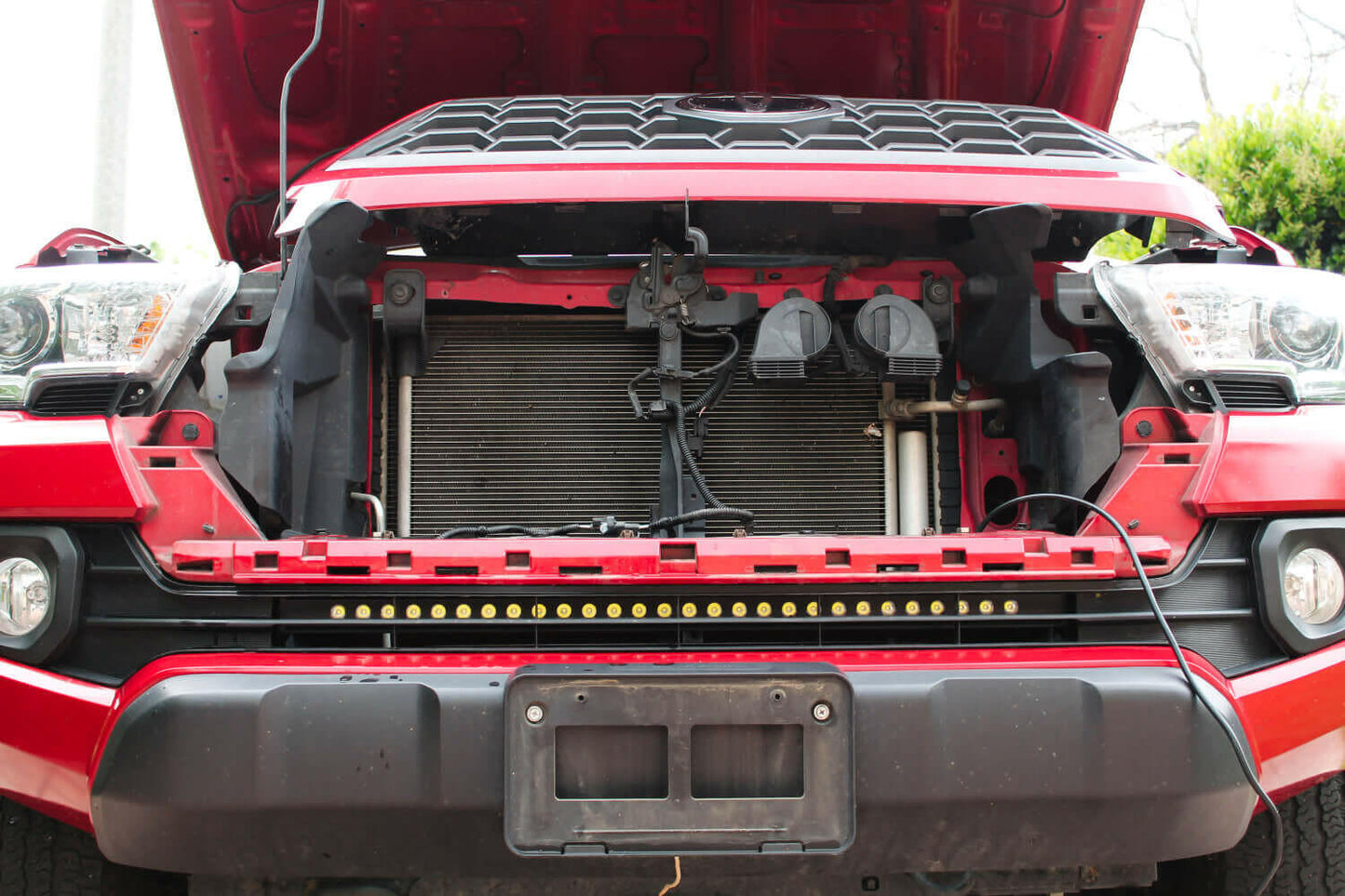 Open hood of a red vehicle showing the engine compartment and mounted light bar.