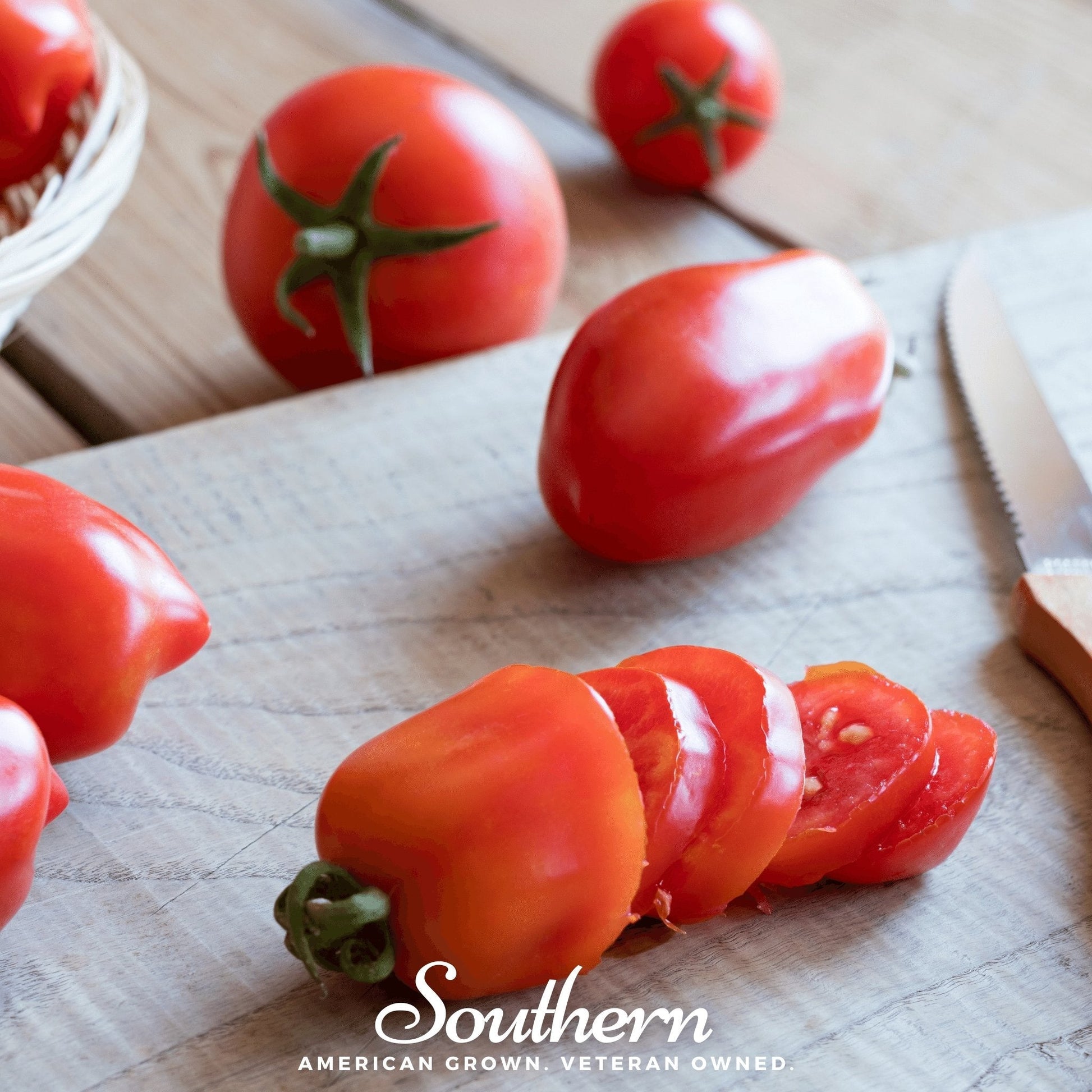 Sliced sauce tomatoes on a wooden cutting board with a knife, surrounded by whole tomatoes.