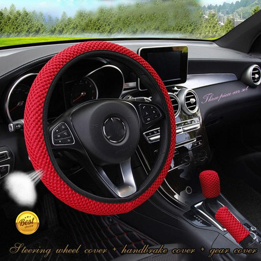 Car interior with a red steering wheel cover and gear shift cover, set against a blurred outdoor background.