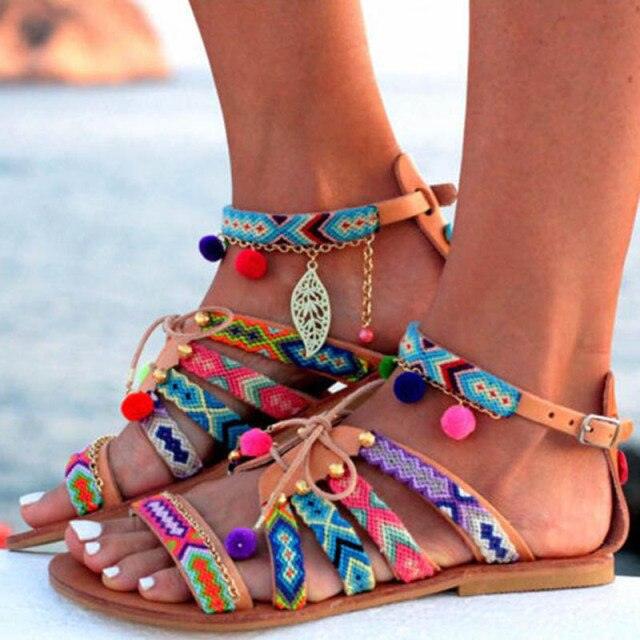 Colorful sandals with decorative straps and pom-poms on a blurred beach background